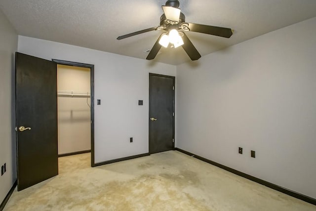 unfurnished bedroom with a closet, a walk in closet, a textured ceiling, light colored carpet, and ceiling fan