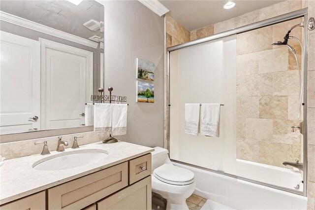 full bathroom featuring bath / shower combo with glass door, crown molding, toilet, vanity with extensive cabinet space, and tile flooring