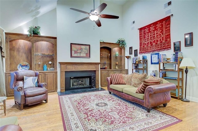 living room with a high ceiling, ceiling fan, and light wood-type flooring