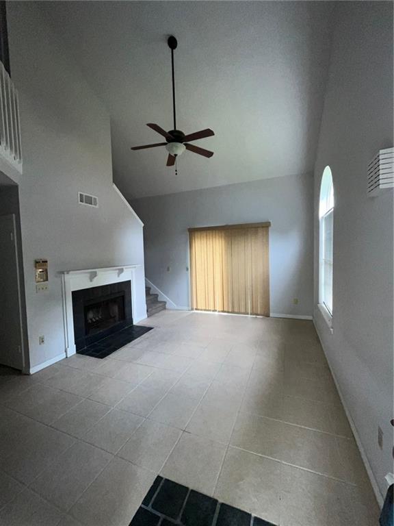 unfurnished living room with high vaulted ceiling, ceiling fan, and tile flooring