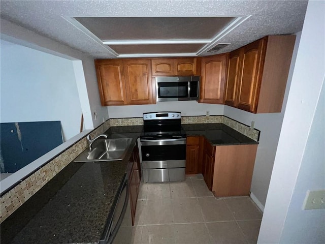 kitchen featuring light tile flooring, appliances with stainless steel finishes, sink, dark stone countertops, and a textured ceiling