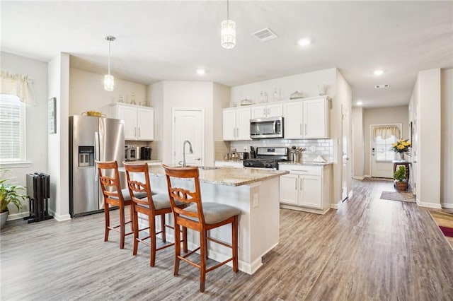 kitchen with stainless steel appliances, a center island with sink, light wood-type flooring, and pendant lighting