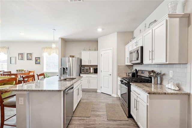 kitchen with a center island with sink, appliances with stainless steel finishes, white cabinets, hardwood / wood-style floors, and backsplash