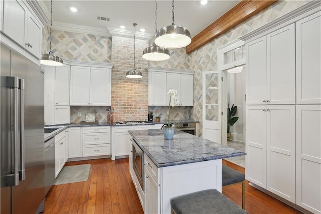 kitchen with appliances with stainless steel finishes, tasteful backsplash, a center island, and hardwood / wood-style flooring