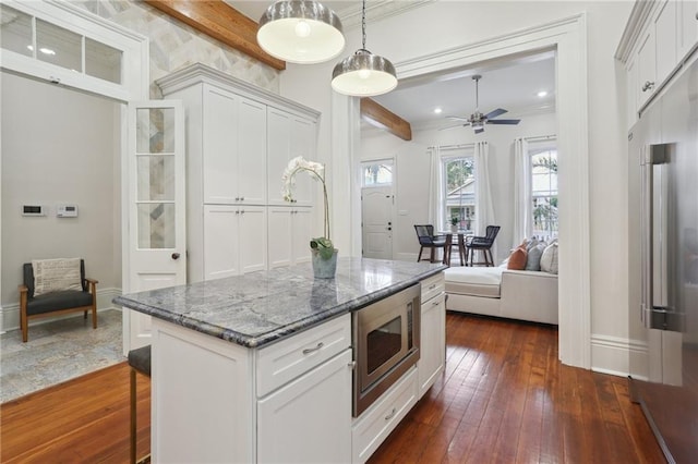 kitchen with stainless steel microwave, decorative light fixtures, beam ceiling, dark hardwood / wood-style floors, and dark stone countertops