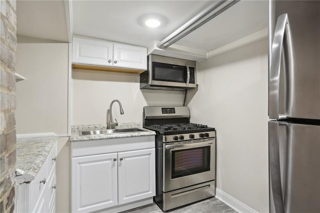 kitchen with sink, stainless steel appliances, light stone countertops, and white cabinetry