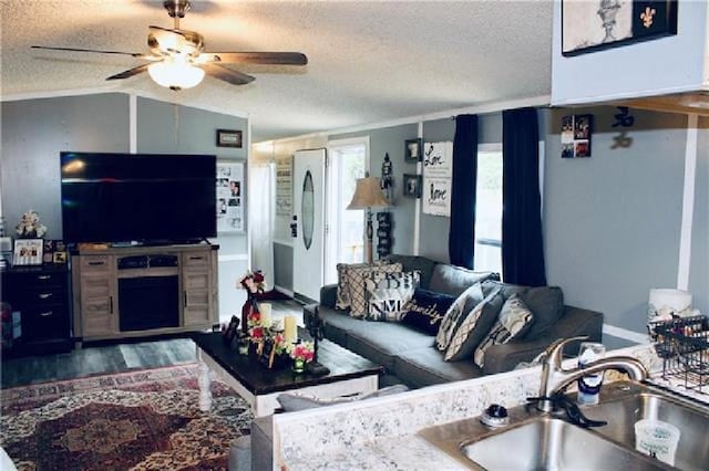 living area with a textured ceiling, vaulted ceiling, wood finished floors, and a ceiling fan