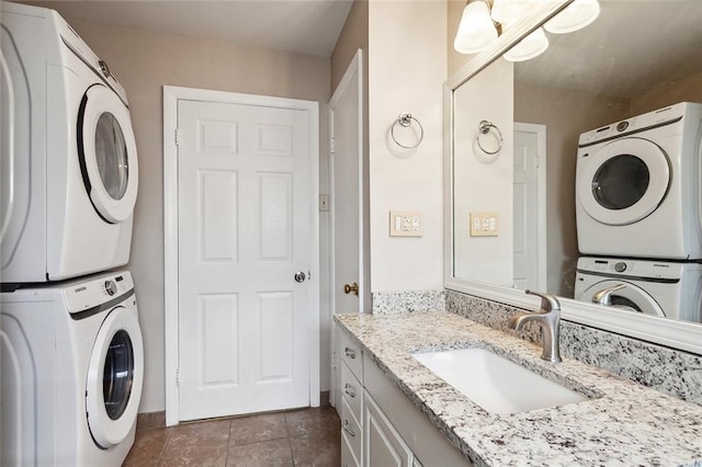 laundry area with dark tile floors, stacked washer / dryer, and sink