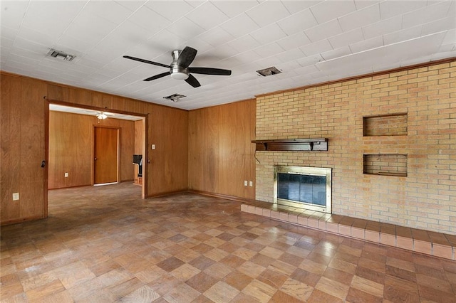 unfurnished living room featuring wooden walls, brick wall, a brick fireplace, and ceiling fan