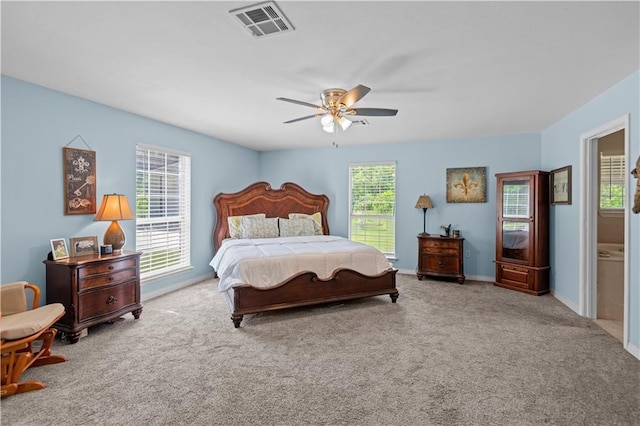 carpeted bedroom featuring multiple windows, ceiling fan, and ensuite bath