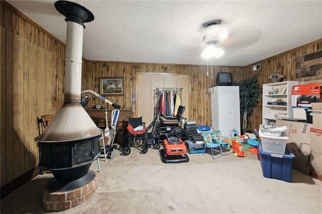 interior space featuring wood walls, a wood stove, carpet flooring, ceiling fan, and a textured ceiling