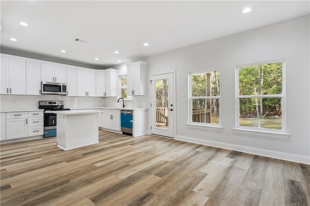 kitchen with appliances with stainless steel finishes, white cabinets, decorative backsplash, a center island, and light hardwood / wood-style flooring