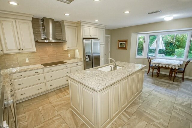 kitchen with sink, wall chimney range hood, tasteful backsplash, stainless steel fridge with ice dispenser, and an island with sink