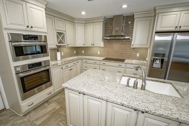 kitchen featuring wall chimney range hood, backsplash, stainless steel appliances, and light stone countertops