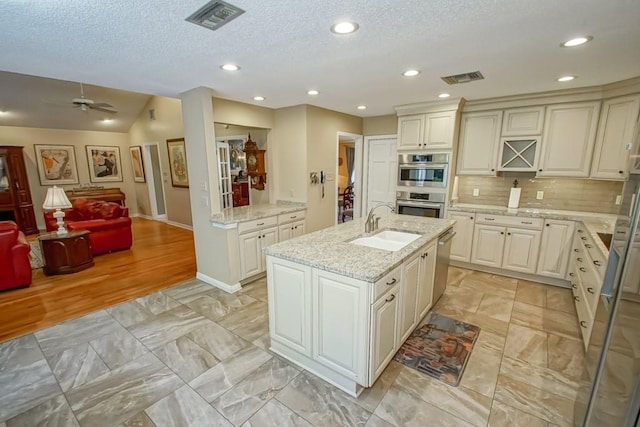 kitchen with appliances with stainless steel finishes, backsplash, a center island with sink, light hardwood / wood-style floors, and sink