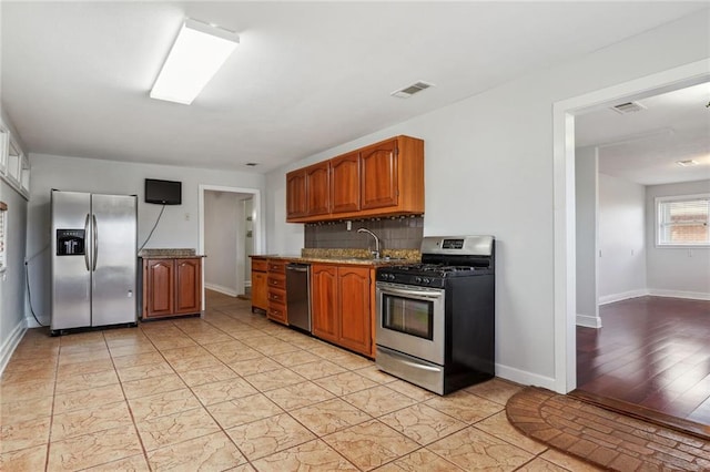 kitchen featuring light stone countertops, stainless steel appliances, tasteful backsplash, sink, and light wood-type flooring