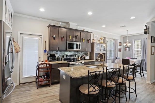 kitchen featuring appliances with stainless steel finishes, light hardwood / wood-style flooring, tasteful backsplash, a kitchen island with sink, and sink