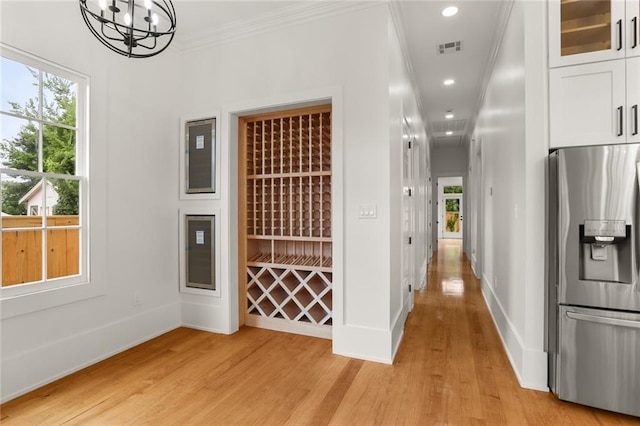 wine area featuring crown molding, a chandelier, and light wood-type flooring