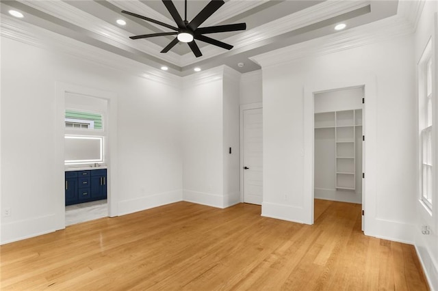 unfurnished bedroom with a walk in closet, a tray ceiling, and light wood-type flooring