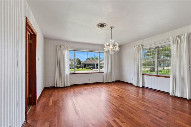 spare room featuring a wealth of natural light, an inviting chandelier, and dark hardwood / wood-style floors