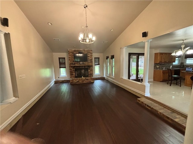 unfurnished living room with high vaulted ceiling, wood-type flooring, ornate columns, a fireplace, and a notable chandelier