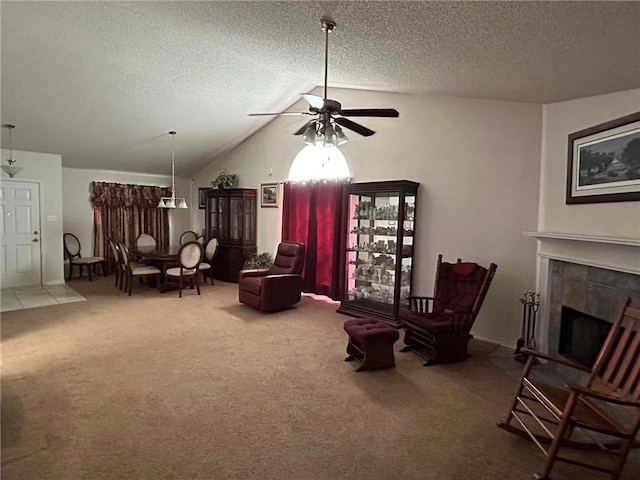 living area featuring ceiling fan, a tile fireplace, a textured ceiling, carpet flooring, and vaulted ceiling