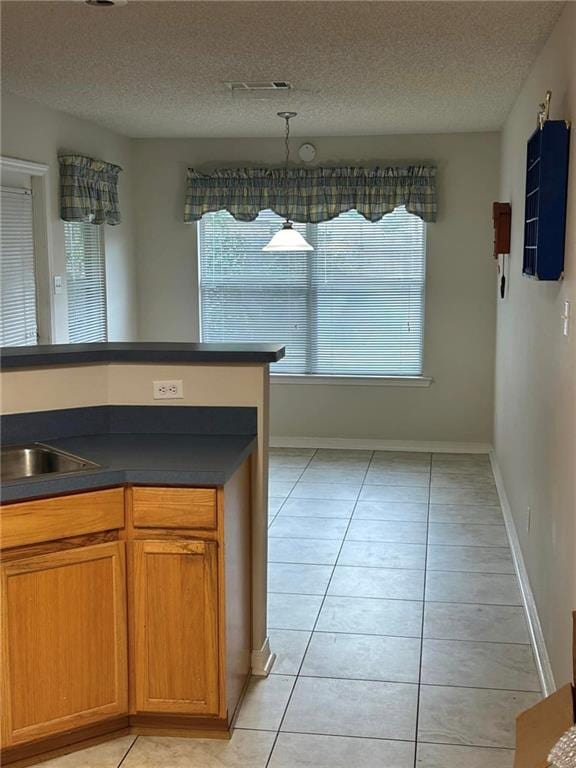 kitchen with a textured ceiling, sink, light tile flooring, and decorative light fixtures