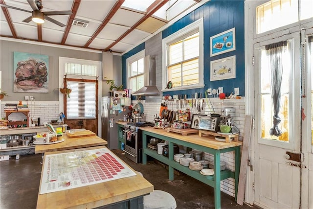 kitchen featuring ceiling fan, stainless steel appliances, and wall chimney range hood