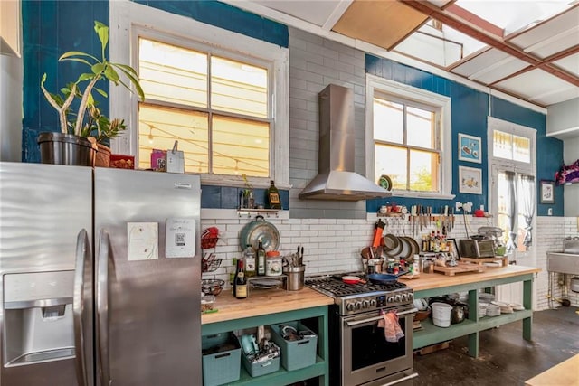 kitchen featuring appliances with stainless steel finishes, wood counters, and wall chimney range hood