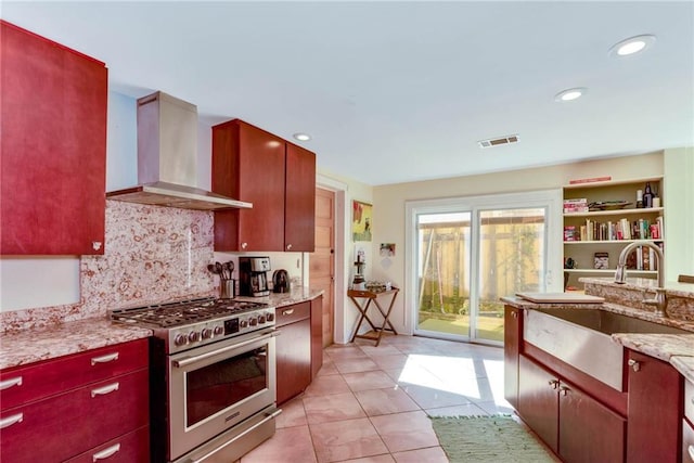 kitchen featuring wall chimney exhaust hood, backsplash, high end stainless steel range, light tile floors, and light stone counters