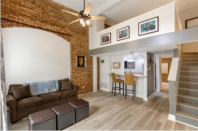 living room with brick wall, light hardwood / wood-style flooring, ceiling fan, and high vaulted ceiling