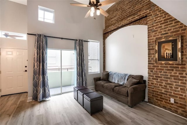 living room with wood-type flooring, a wealth of natural light, ceiling fan, and brick wall