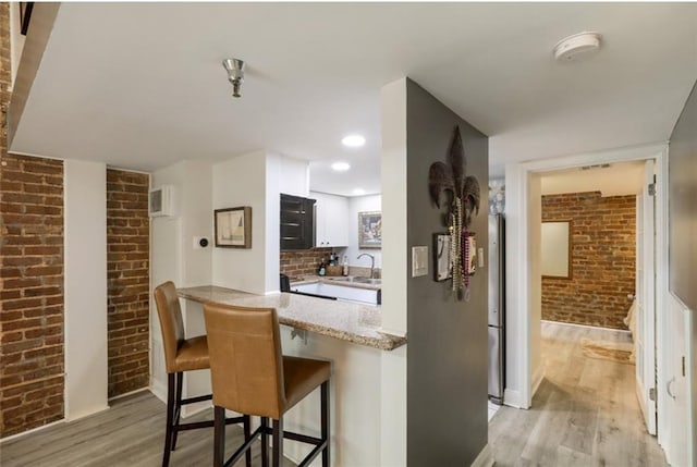 kitchen with light stone counters, kitchen peninsula, sink, a kitchen bar, and light hardwood / wood-style floors