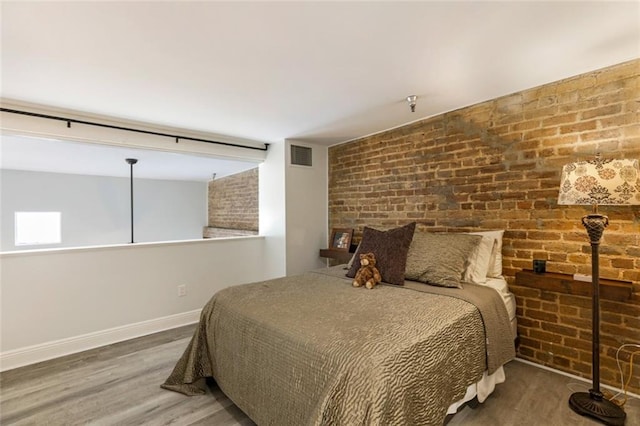 bedroom featuring brick wall and dark hardwood / wood-style floors