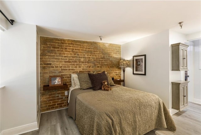 bedroom featuring brick wall and hardwood / wood-style flooring