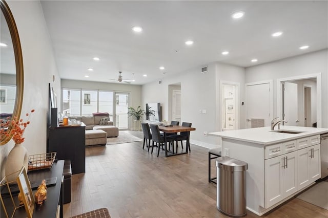 kitchen with ceiling fan, white cabinets, sink, wood-type flooring, and an island with sink