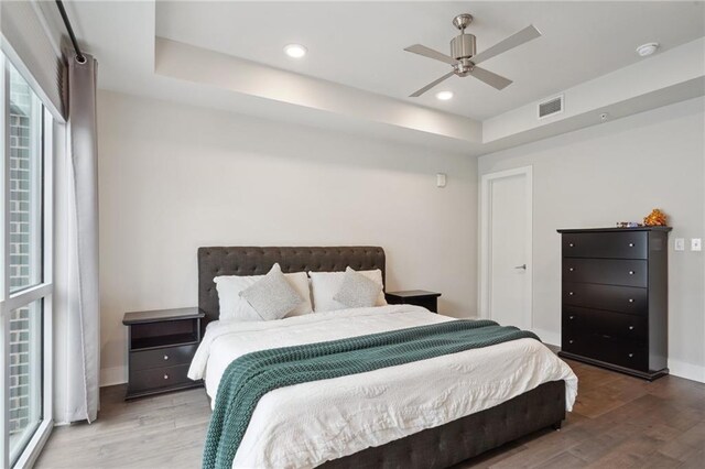 bedroom with hardwood / wood-style flooring, ceiling fan, a raised ceiling, and multiple windows