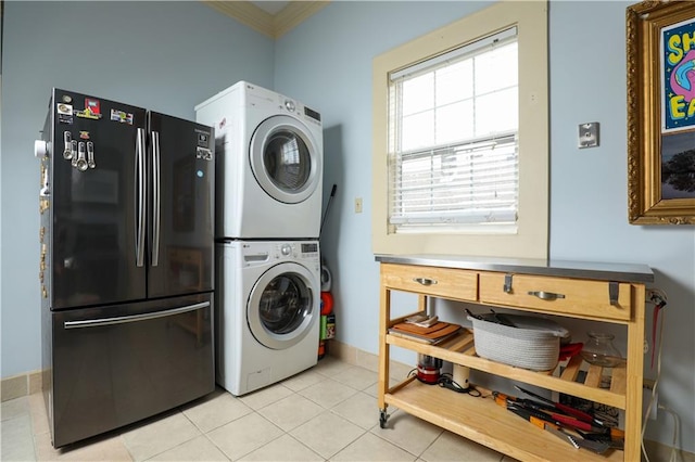 clothes washing area featuring ornamental molding, stacked washer and dryer, and light tile flooring