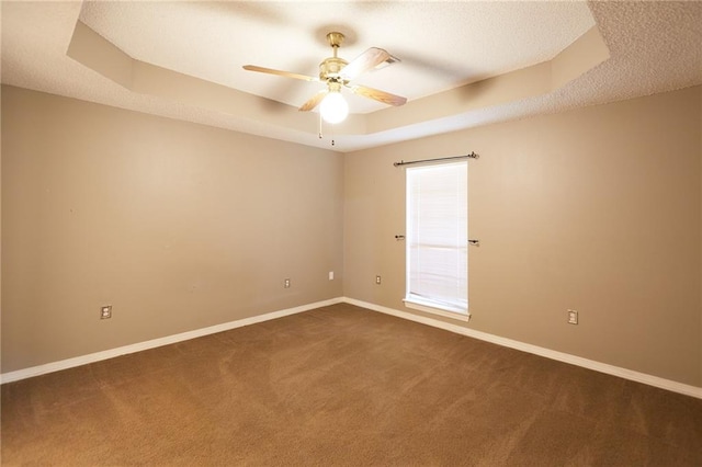 unfurnished room with dark colored carpet, ceiling fan, and a raised ceiling