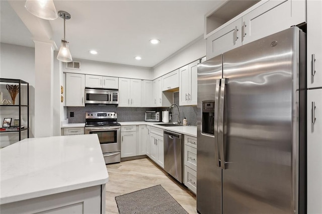 kitchen with appliances with stainless steel finishes, sink, light hardwood / wood-style floors, tasteful backsplash, and pendant lighting