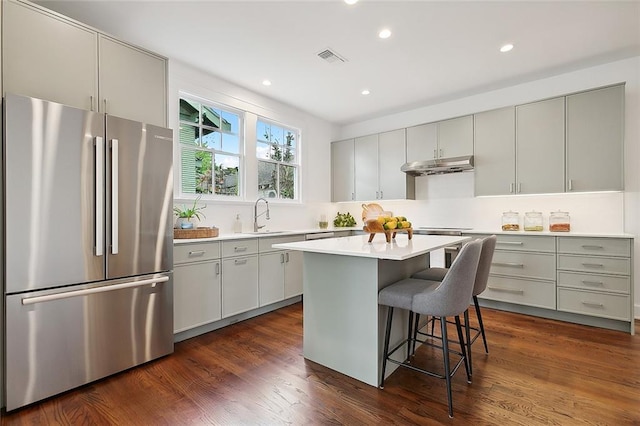 kitchen with a kitchen breakfast bar, dark hardwood / wood-style floors, sink, a kitchen island, and stainless steel fridge