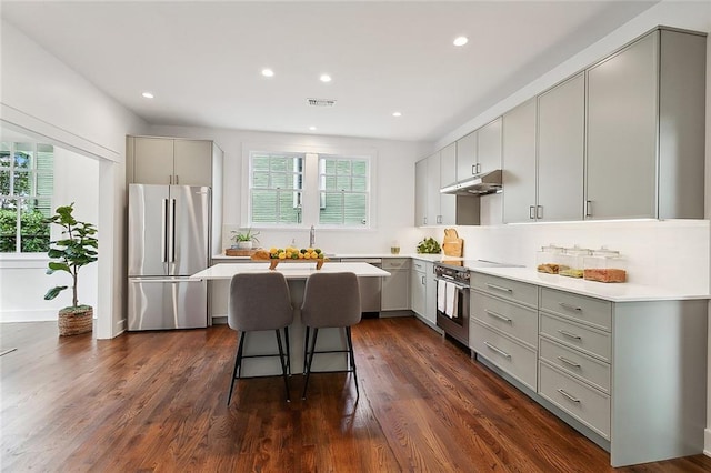 kitchen featuring a kitchen island, a breakfast bar, oven, dark wood-type flooring, and stainless steel fridge