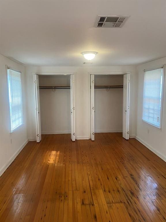 unfurnished bedroom with multiple closets, hardwood / wood-style floors, and multiple windows