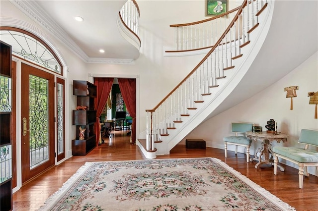 foyer entrance with a towering ceiling, wood-type flooring, crown molding, and a healthy amount of sunlight