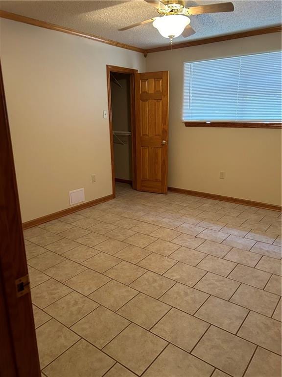 unfurnished room with light tile floors, ornamental molding, ceiling fan, and a textured ceiling