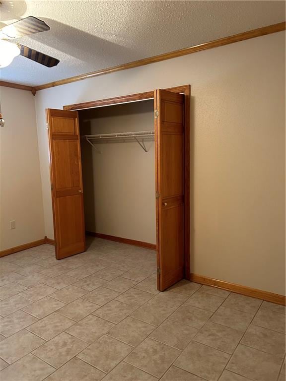 unfurnished bedroom featuring ceiling fan, a closet, crown molding, light tile flooring, and a textured ceiling