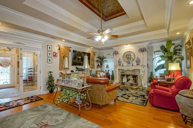 living room with a premium fireplace, ceiling fan, hardwood / wood-style flooring, a raised ceiling, and ornamental molding