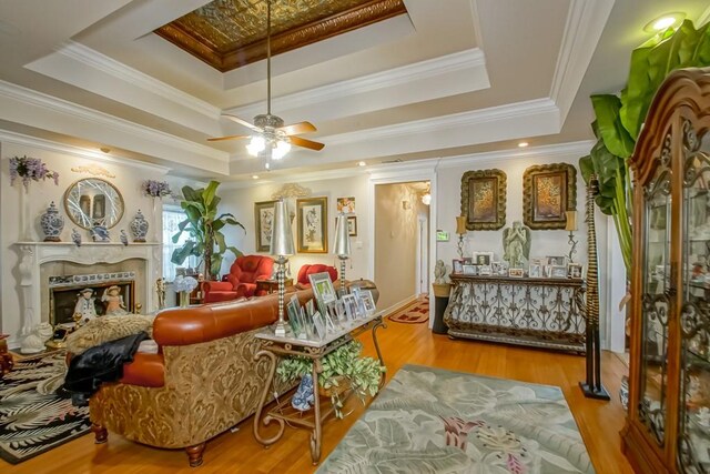 interior space featuring a tray ceiling, ornamental molding, a high end fireplace, light hardwood / wood-style floors, and ceiling fan