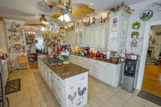 kitchen with light tile floors, ceiling fan with notable chandelier, decorative light fixtures, ornamental molding, and stainless steel gas cooktop