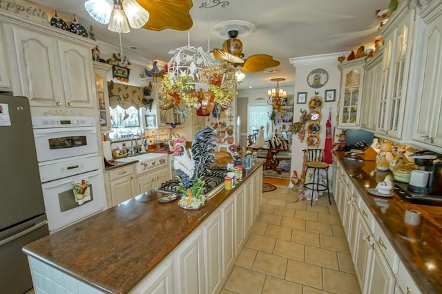 kitchen featuring decorative light fixtures, light tile flooring, ceiling fan with notable chandelier, stainless steel fridge, and a center island